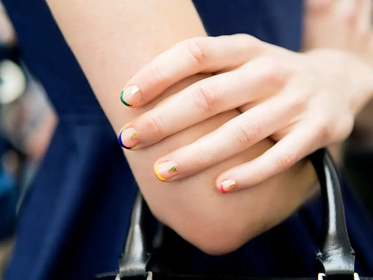 Manicura geométrica con colores vibrantes y detalles dorados en uñas cortas bonitas.