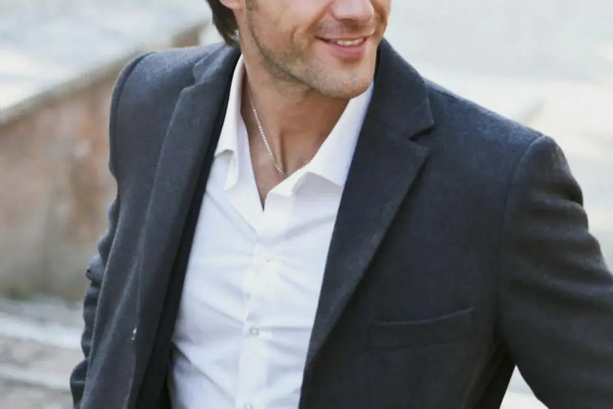 Hombre sonriente con chaqueta gris y camisa blanca, luciendo un estilo look smart casual.