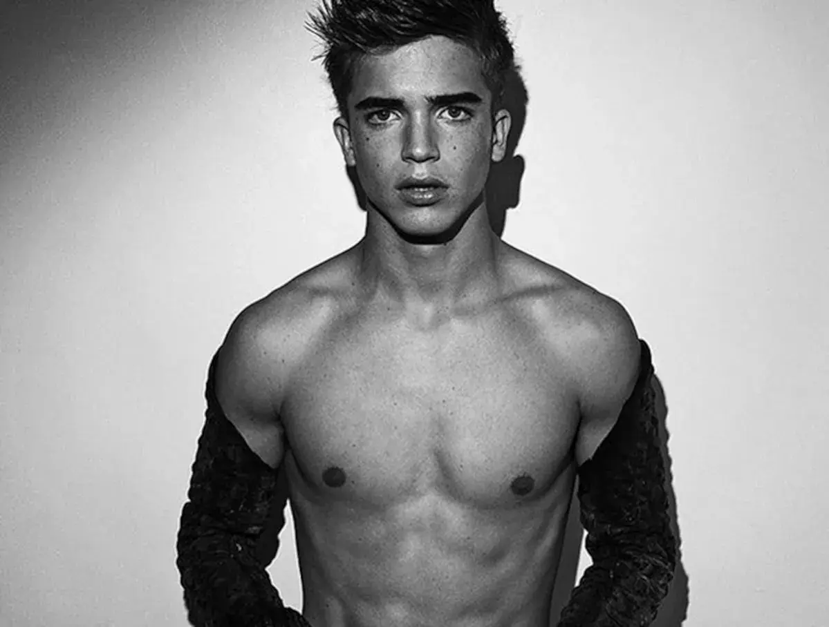 Joven modelo hombre con mirada intensa, torso descubierto y mangas oscuras.