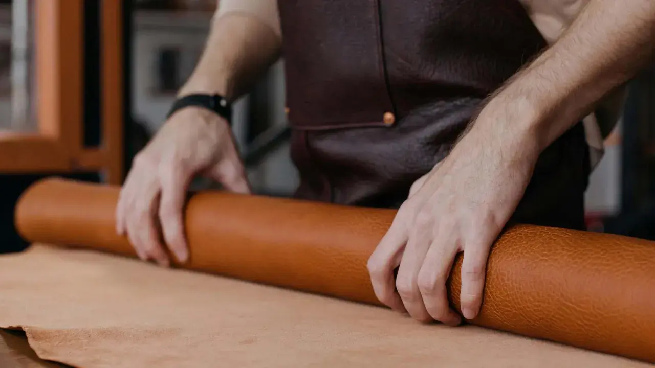 Manos de artesano desenrollando un rollo de cuero, mostrando la textura y el color natural del material. Se pregunta de que esta hecho el cuero.