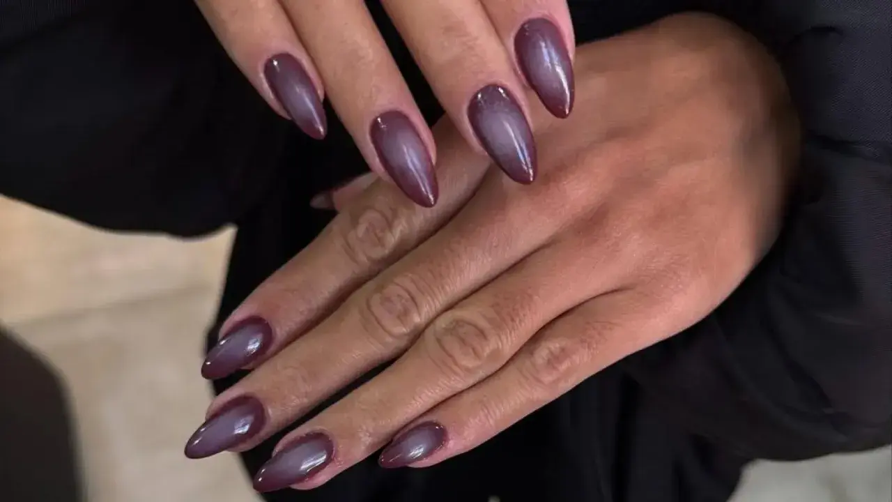 Manicura con uñas almendradas en tono morado oscuro, con un efecto degradado que recuerda a las aura nails.