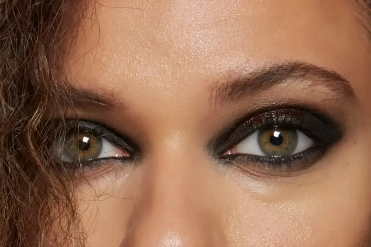 Ojos con un intenso smokey eye en tonos oscuros, delineado marcado y pestañas voluminosas.