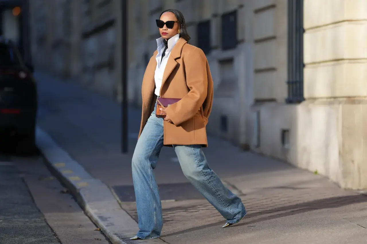 Mujer con abrigo camel, camisa blanca y jeans anchos, luciendo un bolso morado. Su estilo es muy aesthetic.