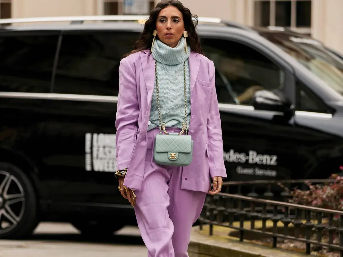 Una mujer luce un traje lila y un suéter azul pálido, demostrando que el azul es un color que combina con el lila.