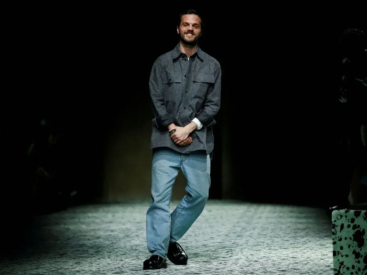 Matthieu Blazy, diseñador de Bottega Veneta, sonríe en la pasarela con camisa gris y vaqueros.
