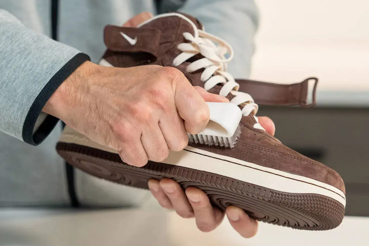 Man limpiando serraje de una zapatilla marrón con un cepillo blanco.