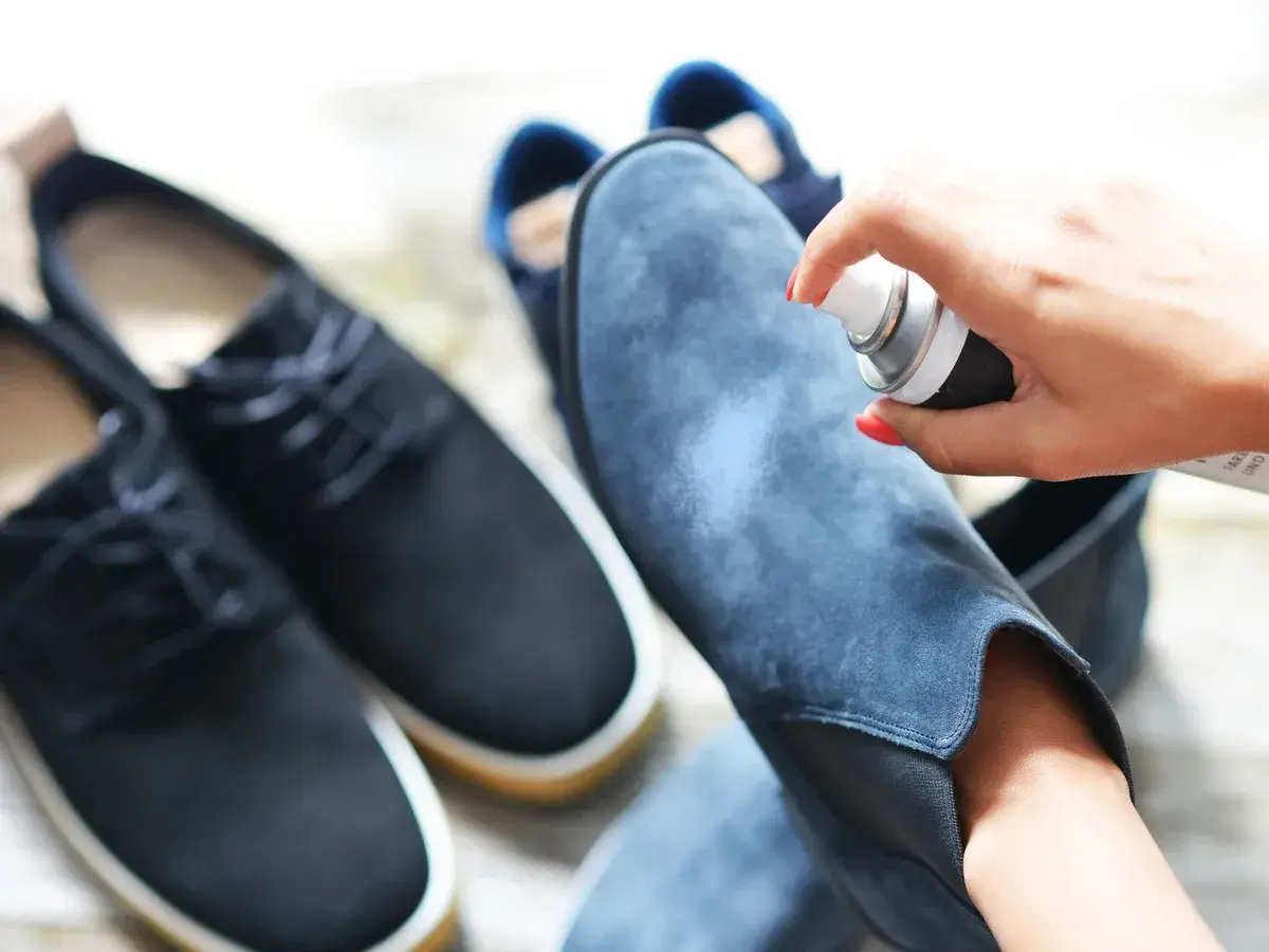 Aplicando spray protector a unas botas de terciopelo azul. Aprende como limpiar botas de terciopelo para mantenerlas como nuevas.
