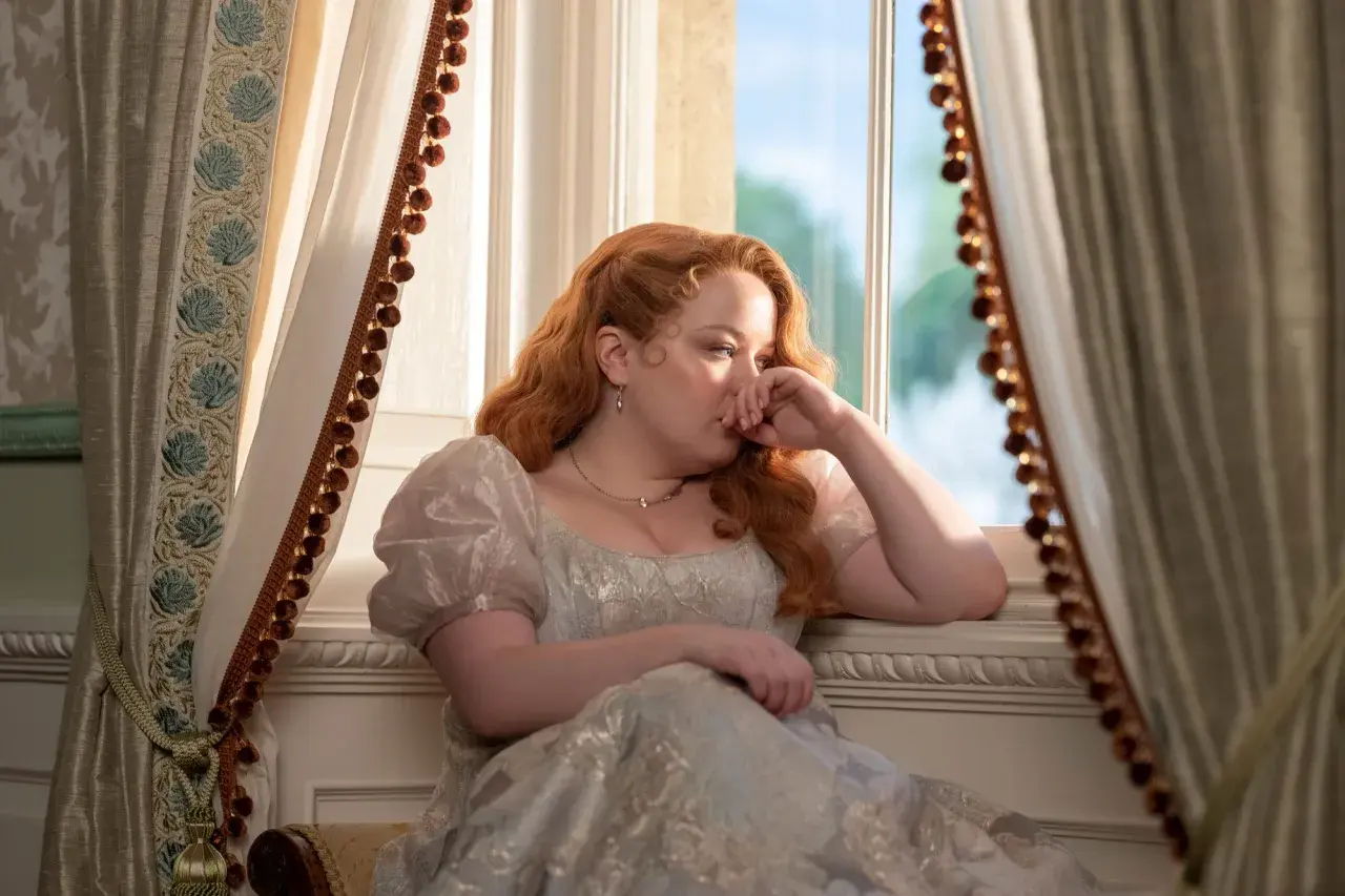 Penelope Bridgerton, la actriz, reflexiona junto a la ventana con un vestido de época.