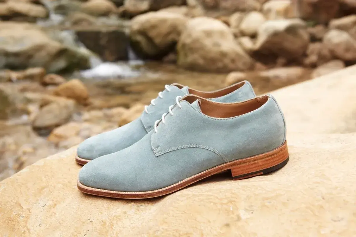 Zapatos de ante azul claro con cordones blancos, descansando sobre rocas junto a un arroyo. ¡Qué ante en zapatos!