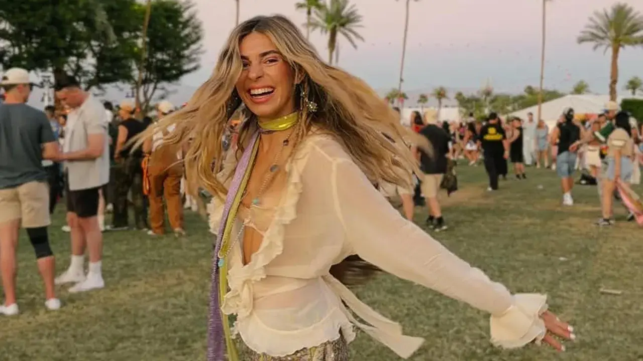 Mujer sonriente y con el pelo al viento disfruta de un look festival verano, rodeada de palmeras y gente.