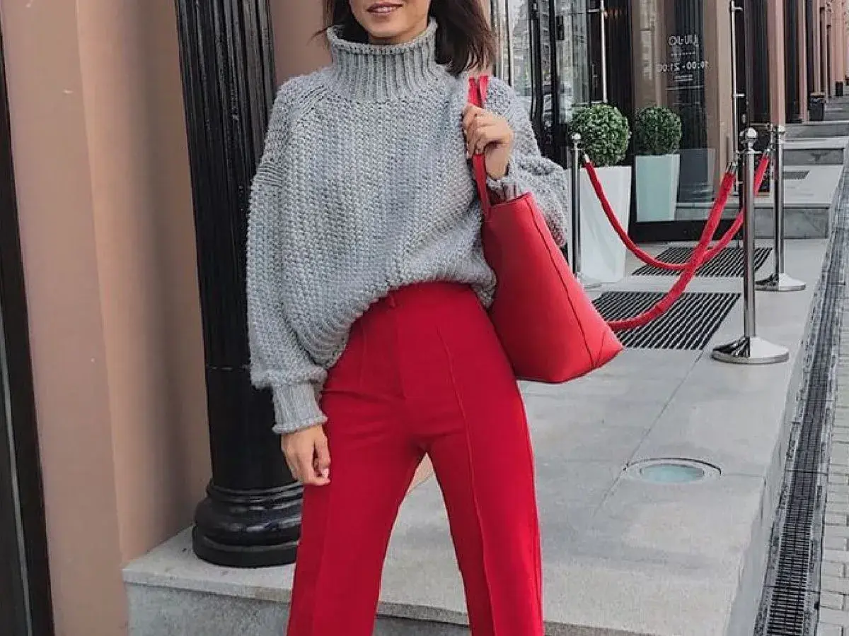 Chaqueta de punto gris y pantalones granate combinan a la perfección. Un bolso rojo vibrante completa el look.