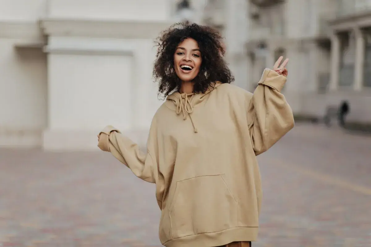 Mujer sonriente con pelo rizado, luciendo un cómodo estilo oversize en sudadera beige.