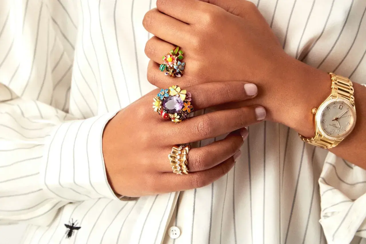 Manos adornadas con anillos florales coloridos y un reloj dorado, luciendo un estilo suot studio.