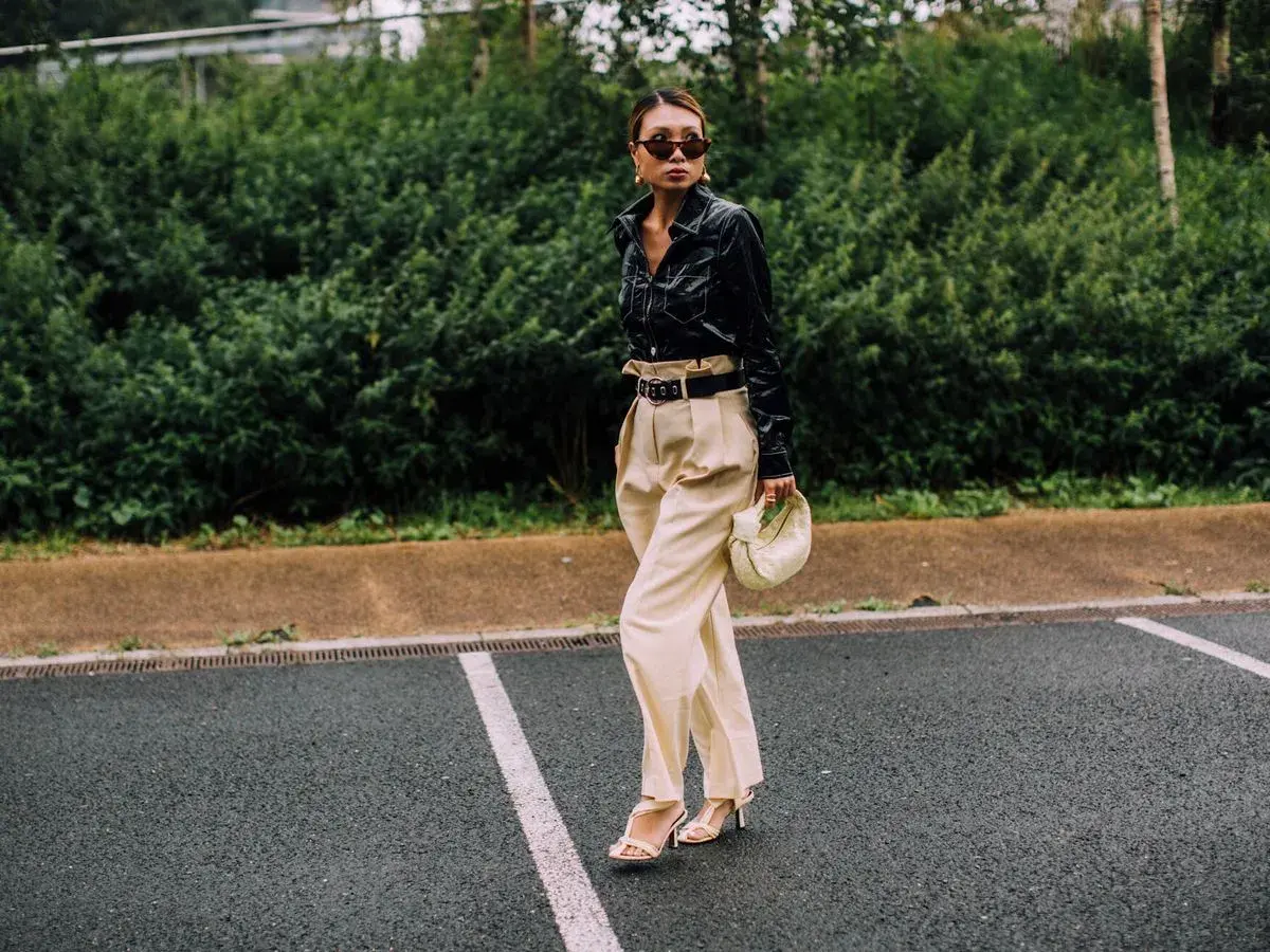Mujer con elegante **pantalón beige** de talle alto, camisa negra brillante y bolso blanco.