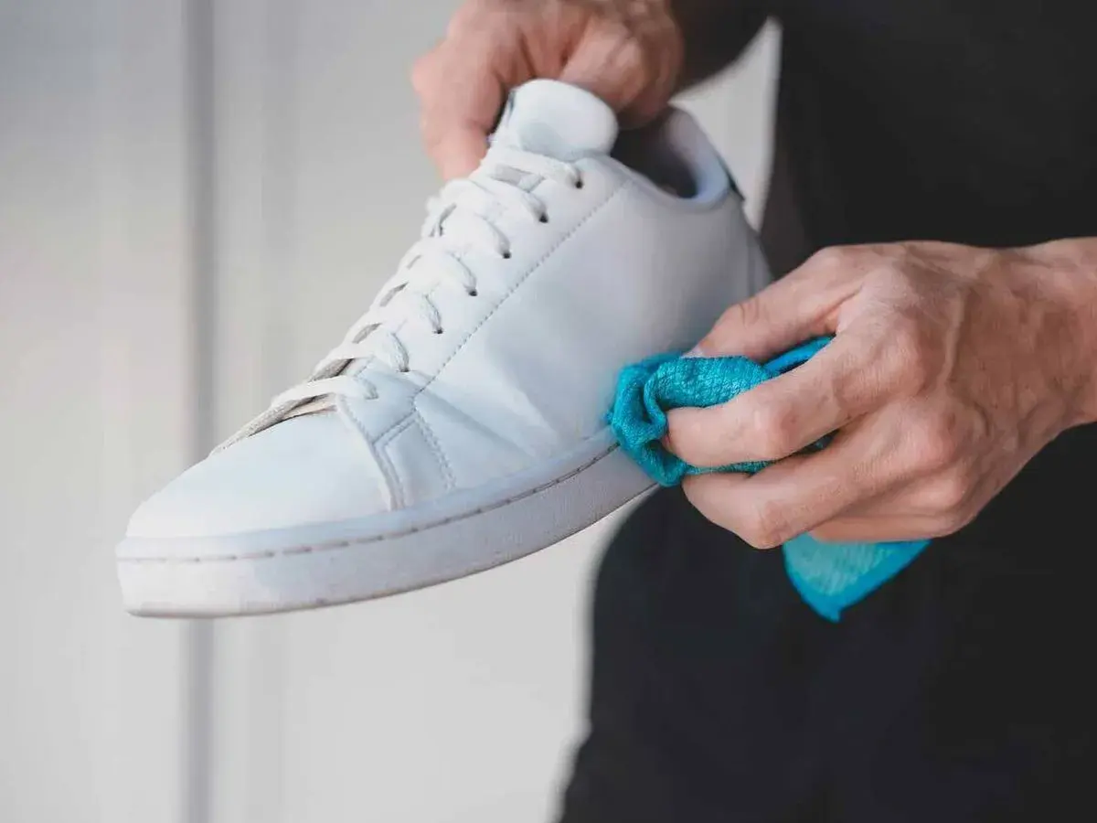 Manos limpiando las gomas de unas zapatillas blancas con un paño azul. Un detalle para saber como limpiar las gomas de las zapatillas y dejarlas como nuevas.