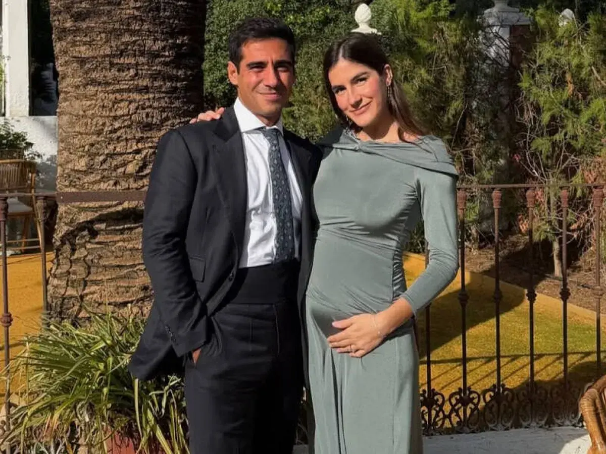 Pareja sonriente, él con traje oscuro, ella con vestido verde ceñido, acariciando su vientre. Blanca Llandres, radiante, espera un bebé.