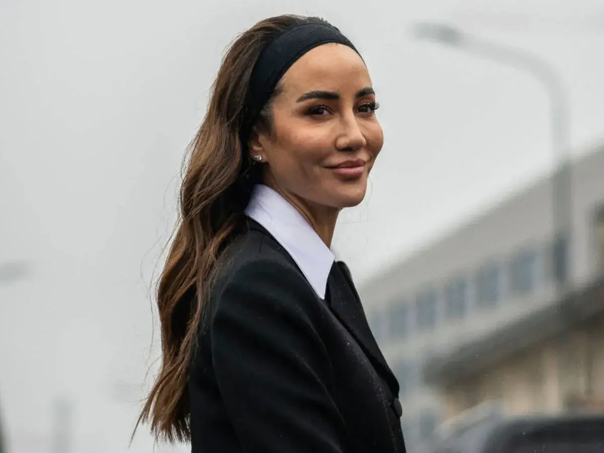 Mujer con peinado con diadema y pelo suelto, luciendo un traje negro y camisa blanca.