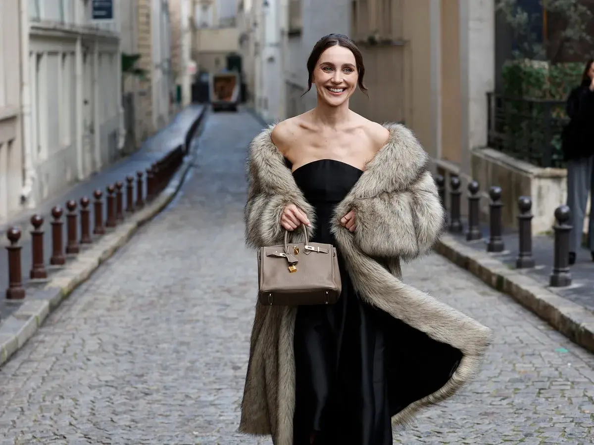 Elegante mujer con abrigo de pelo y bolso, lista para una boda en otoño.