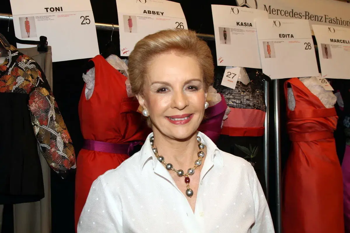Carolina Herrera, icono de la moda, sonríe rodeada de vestidos de pasarela.