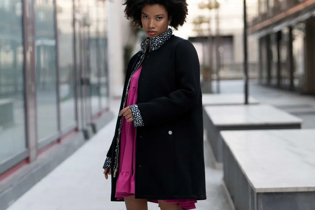 Mujer con estilo urbano y moda oversize, luce un vestido rosa vibrante bajo una chaqueta negra con detalles de lunares.