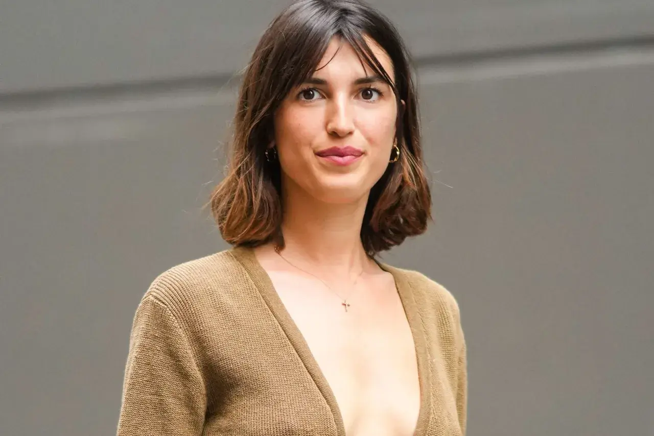 Mujer con cabello castaño ondulado, en transición de pelo corto a largo. Lleva un suéter de punto color camel y un collar con una cruz.