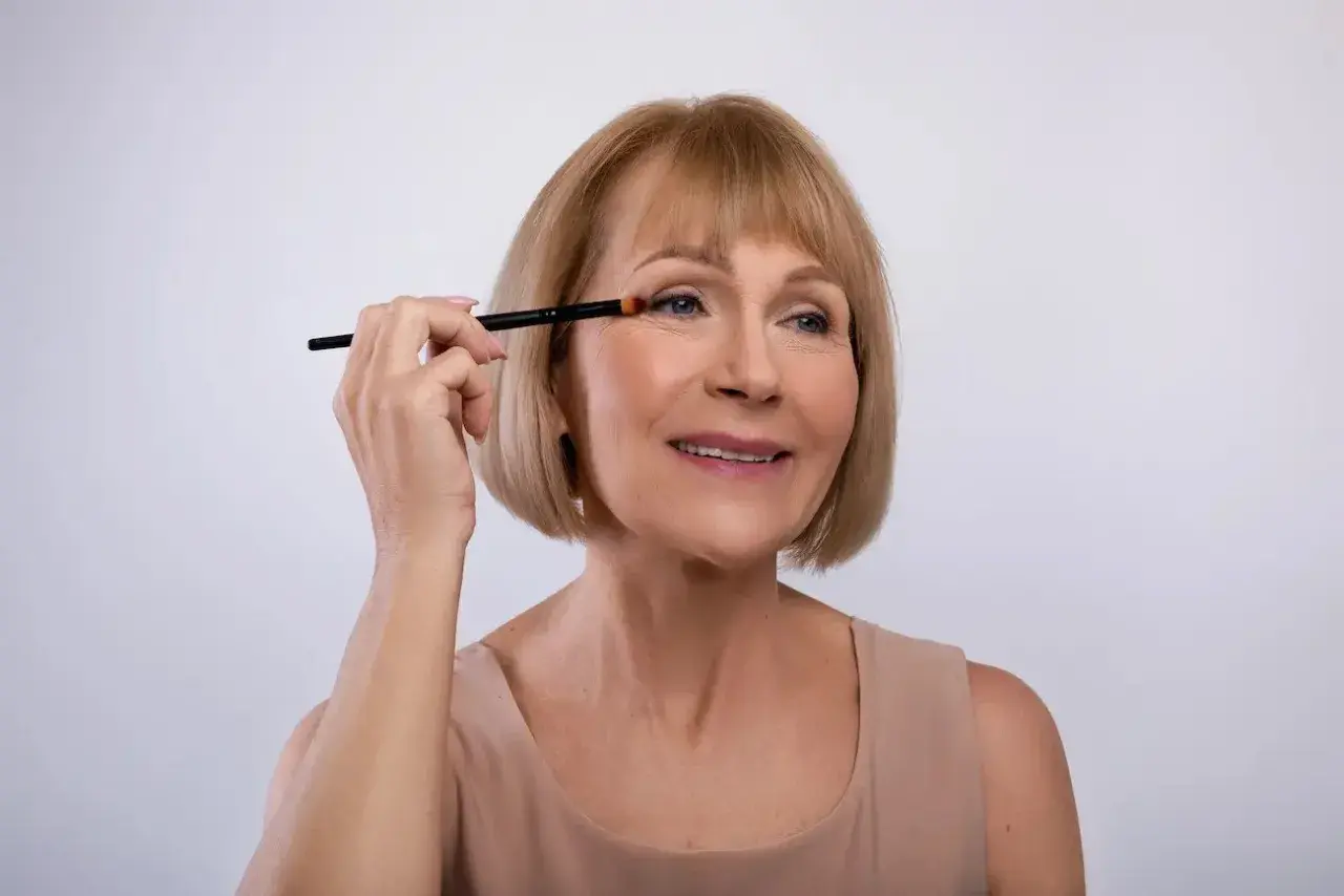 Mujer mayor aplicando sombra de ojos con brocha, aprendiendo como maquillar los ojos a partir de los 50 años para realzar su belleza natural.
