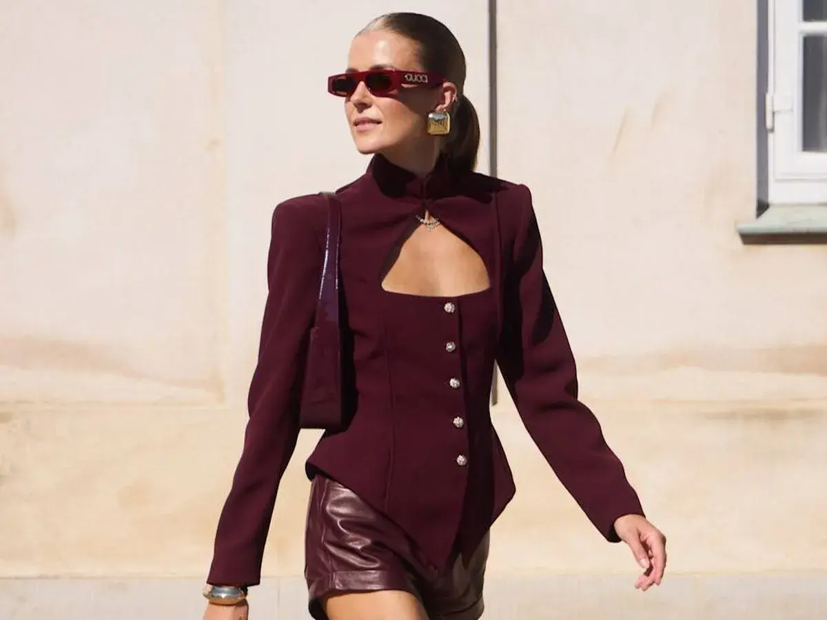 Mujer con gafas rojas y chaqueta granate con escote, combinando granate y rosa en su look audaz.