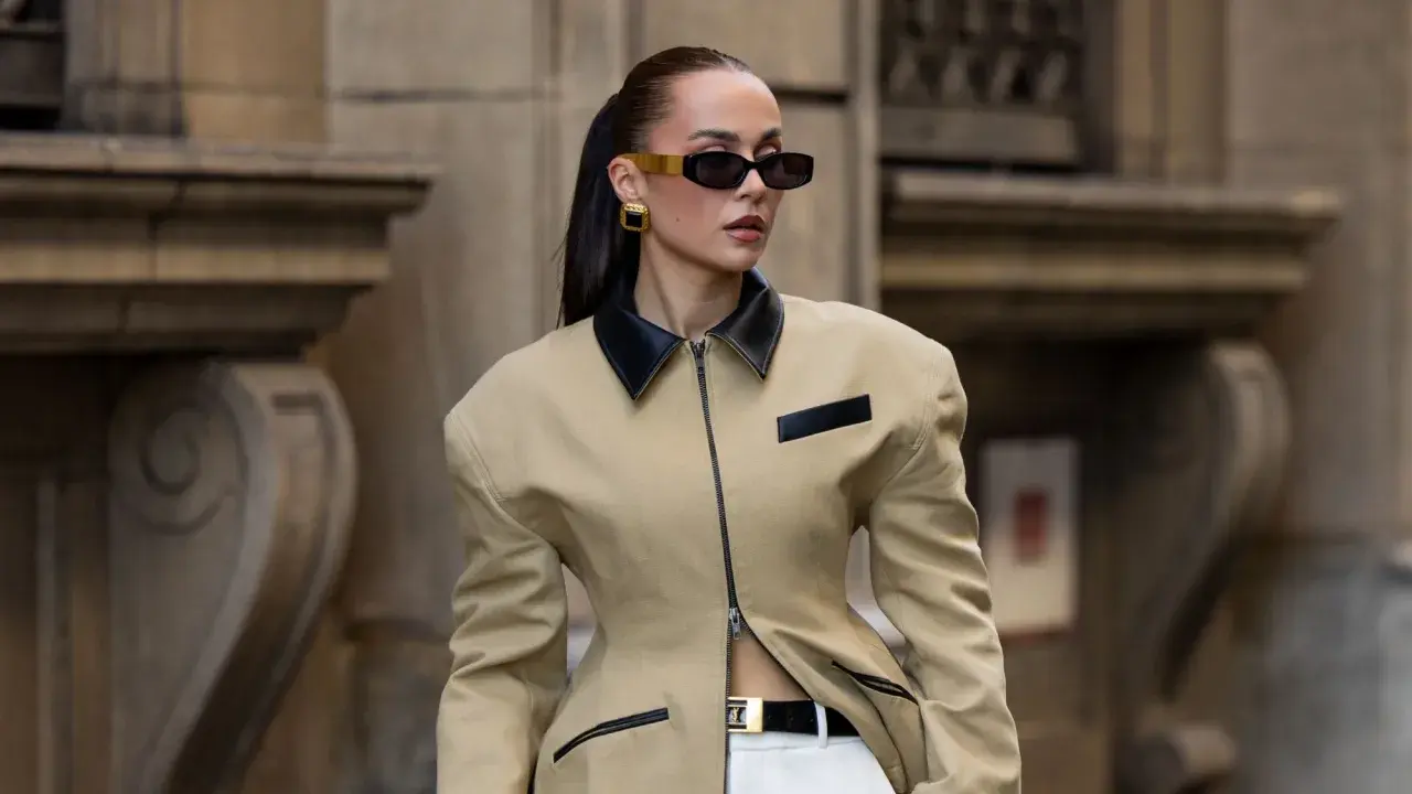 Mujer con gafas de sol y chaqueta beige con cuello negro, luciendo un look de street style impecable.