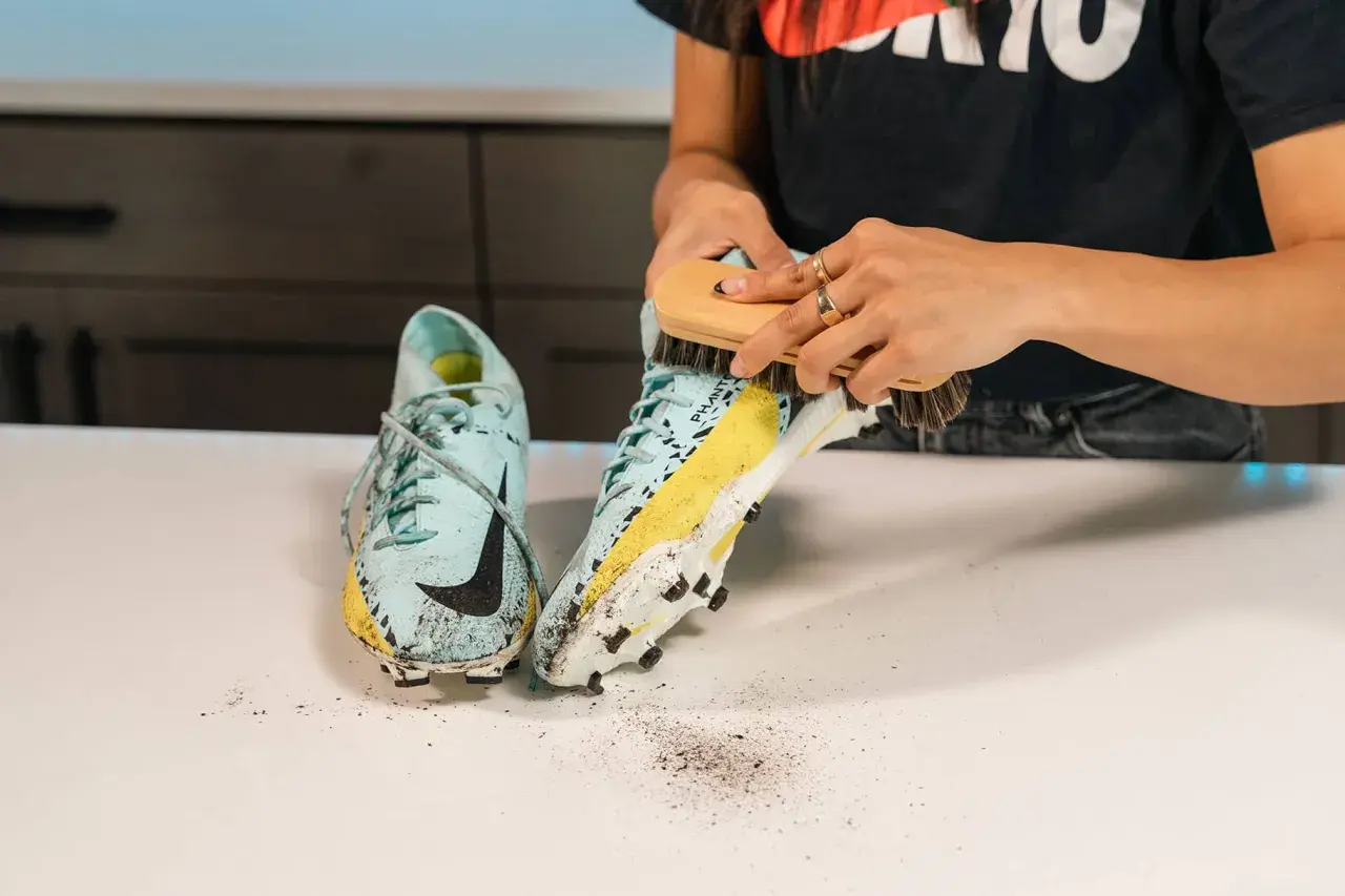 Manos cepillando unas botas de fútbol sucias para aprender como lavar las botas de futbol.