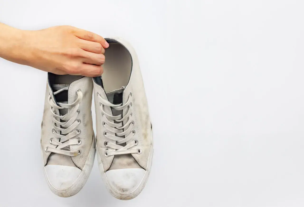 Mano sosteniendo un par de zapatillas blancas de tela sucias, listas para limpiar.