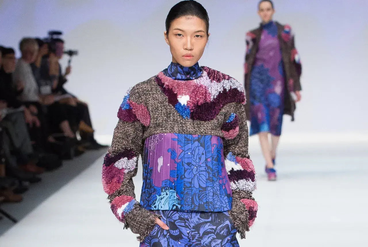 Modelo luce un diseño de upcycling que es una explosión de texturas y colores, con un suéter de tweed y apliques peludos sobre un vestido estampado floral.