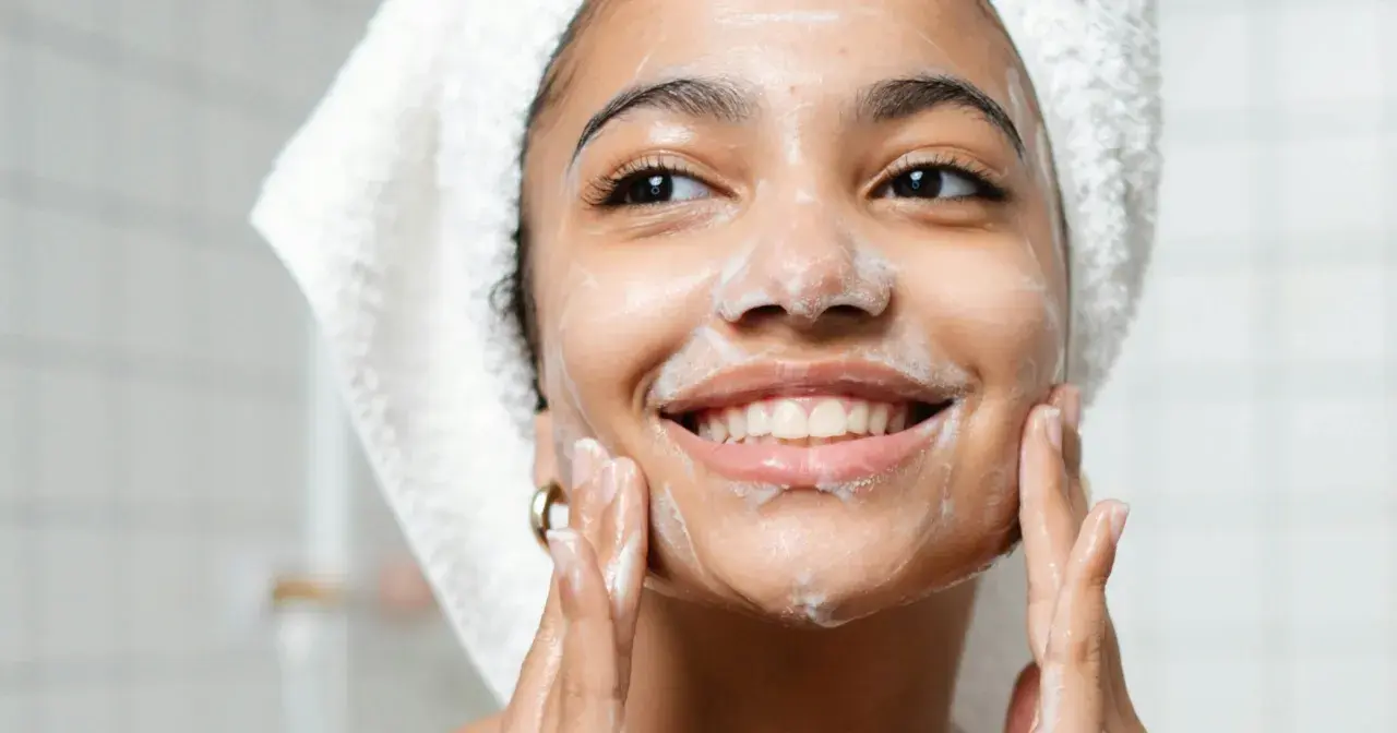 Mujer sonriente con espuma en el rostro, disfrutando de su rutina de doble limpieza facial.
