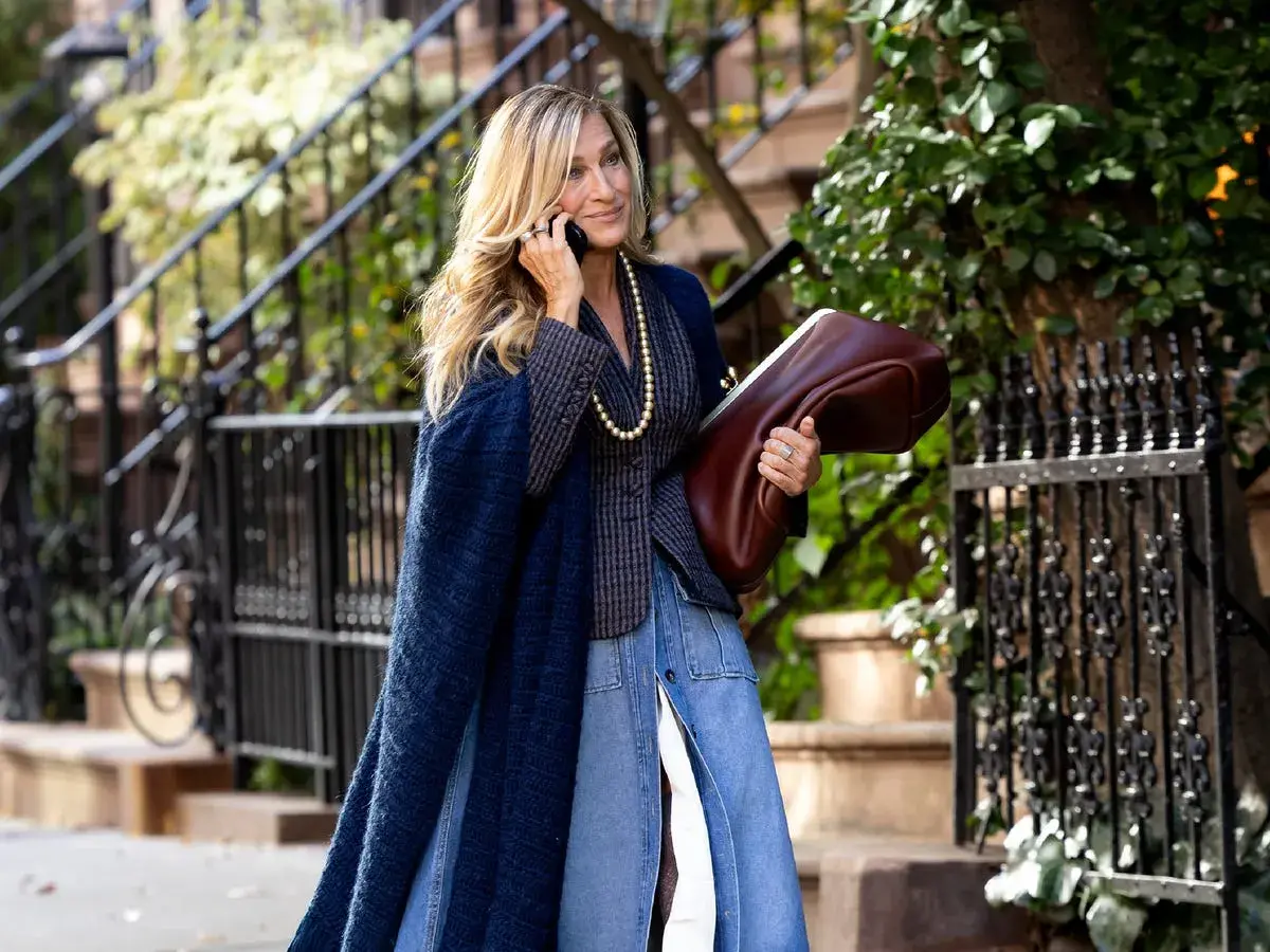 Estilo chic en la ciudad: una mujer con un abrigo azul marino y falda vaquera, combinando granate y verde con su bolso y el follaje.
