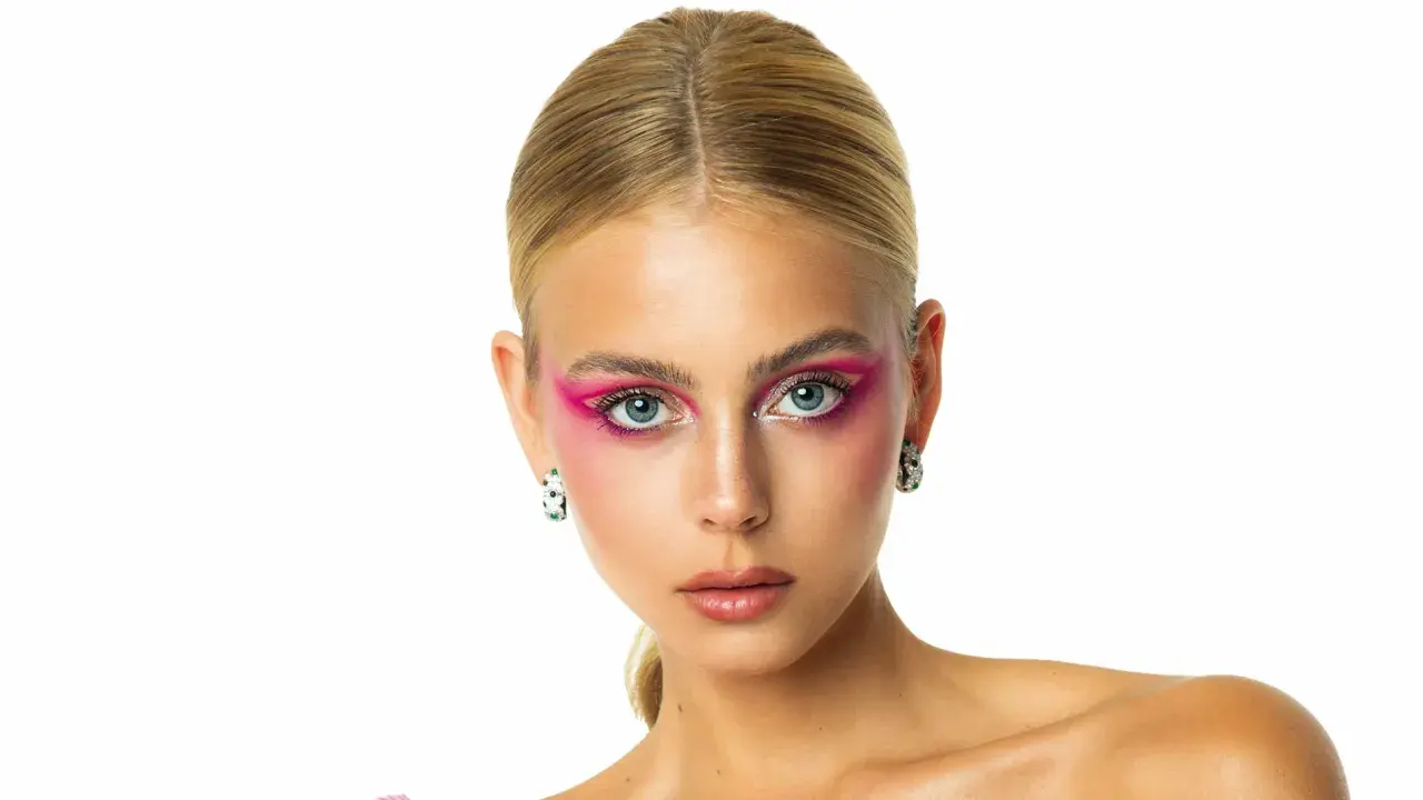 Mishel Gerzig con un audaz maquillaje de ojos rosa vibrante y pendientes llamativos.