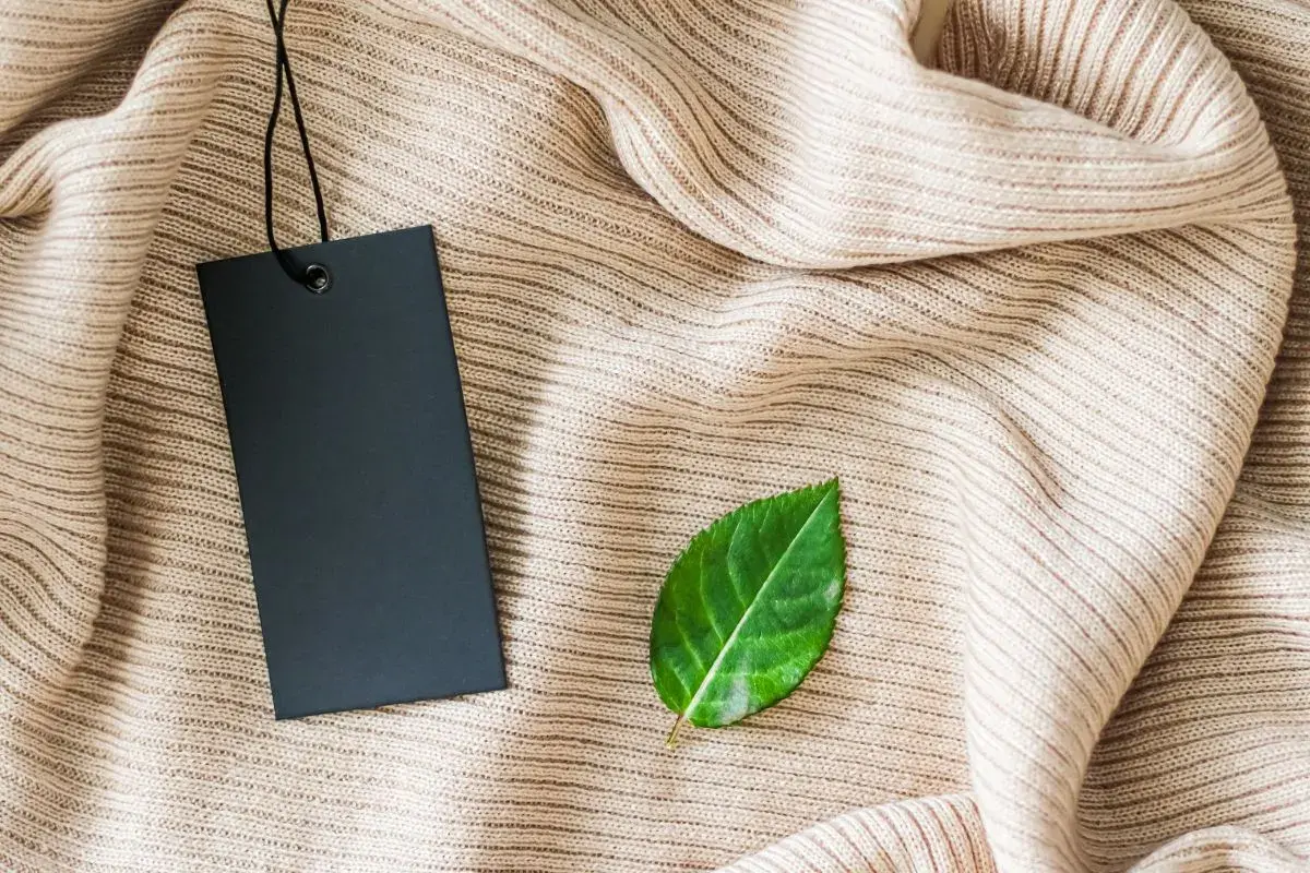 Etiqueta negra sobre tejido beige, con una hoja verde al lado. Símbolo de una marca sostenible.