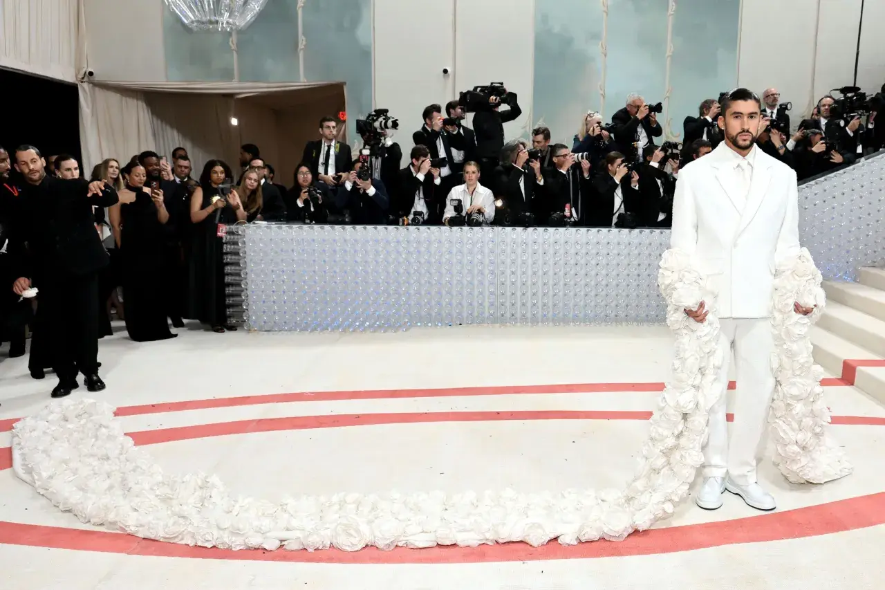 Bad Bunny deslumbra en la Met Gala con un traje blanco adornado con flores, rodeado de fotógrafos.