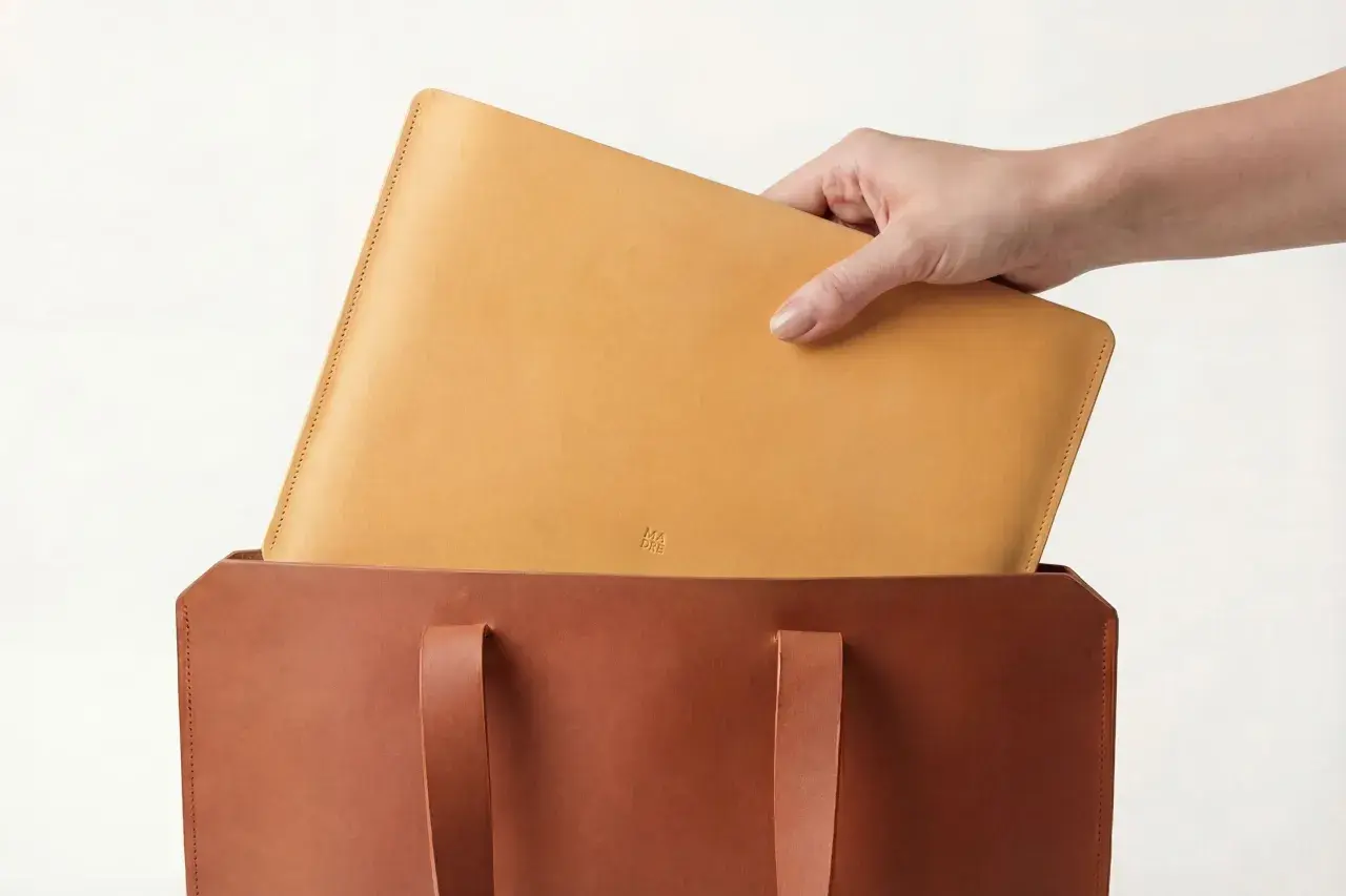 Mano colocando un portátil de piel vegetal en un bolso de cuero.
