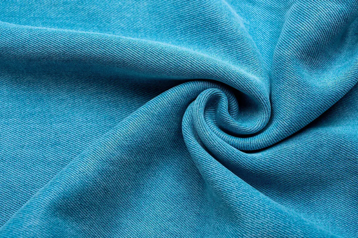 Textura de tela Tencel azul vibrante, suave y con caída, que evoca la comodidad y sostenibilidad de este tejido.
