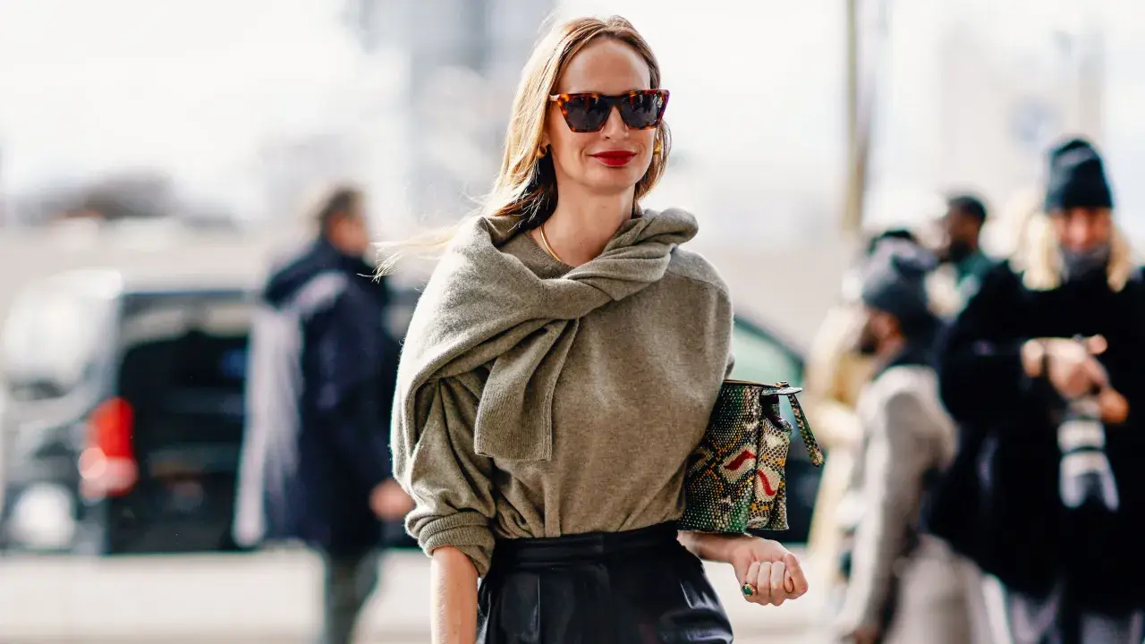 Mujer de unos 40 años con un look casual chic, gafas de sol, suéter gris y bolso estampado.