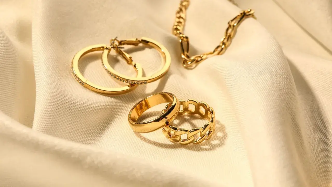 Anillos y cadena dorados sobre tela. Los aros tienen pequeñas piedras preciosas incrustadas, como si fueran diamantes.