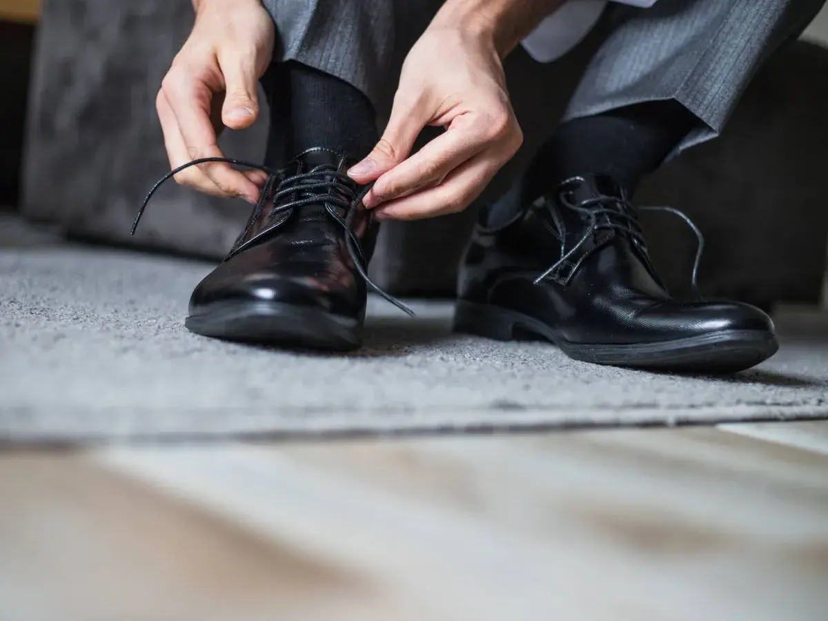 Man se ata los cordones de sus zapatos de piel negros, preparándose para evitar rozaduras.