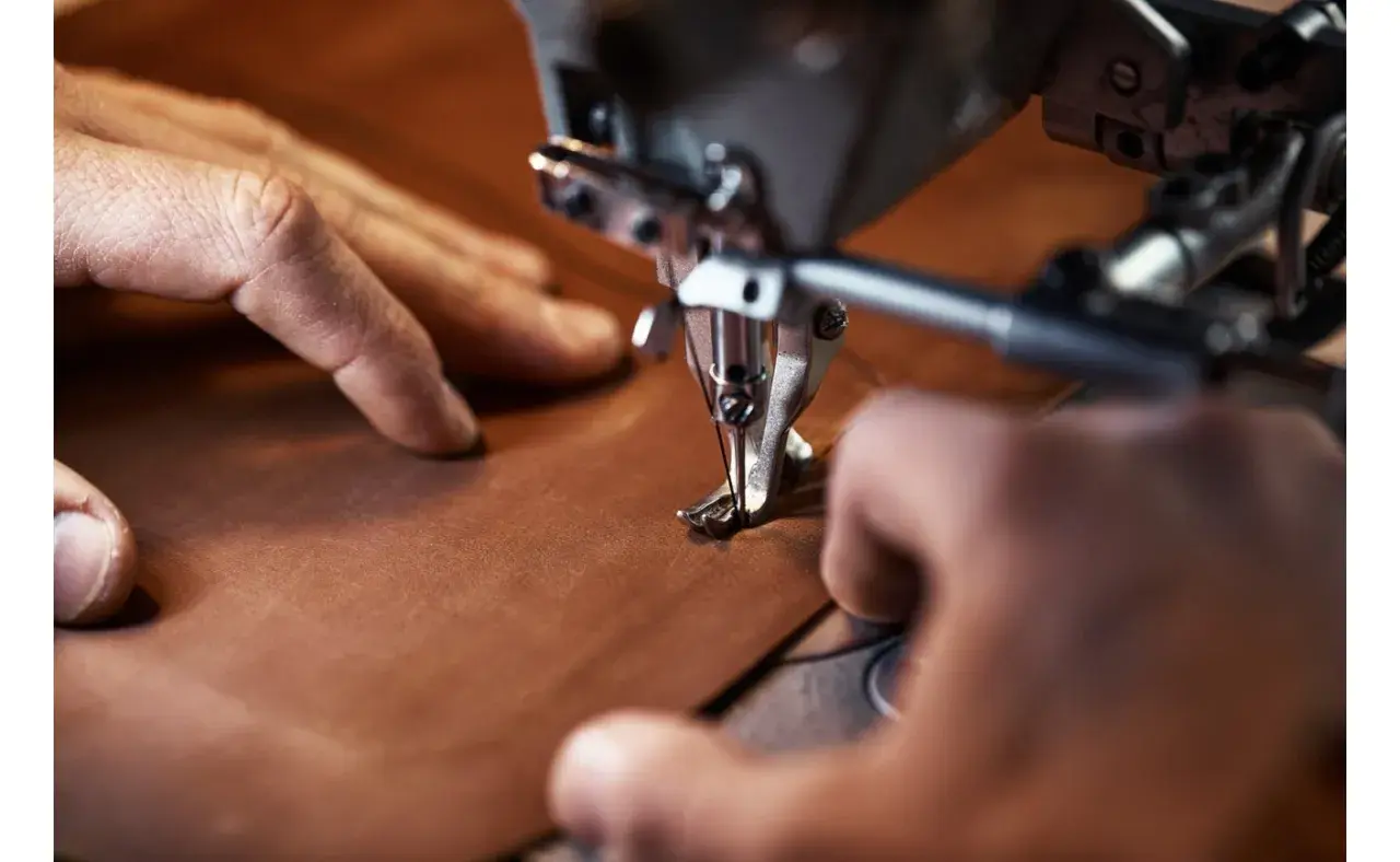 Manos cosiendo con precisión una pieza de cuero vegetal en una máquina de coser industrial.