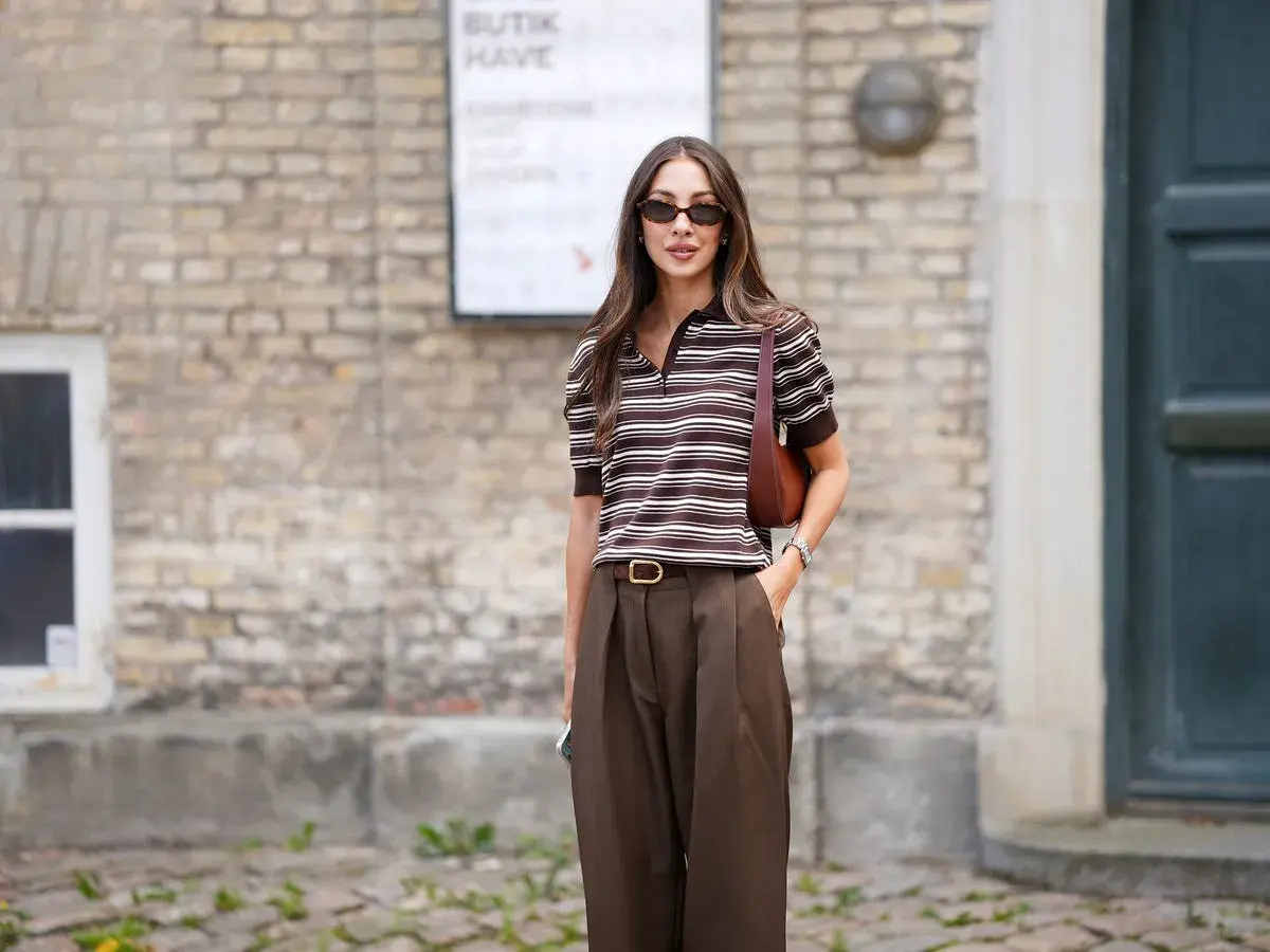 Mujer con estilo, combinando un pantalón marrón de tiro alto con una blusa a rayas marrones y blancas.