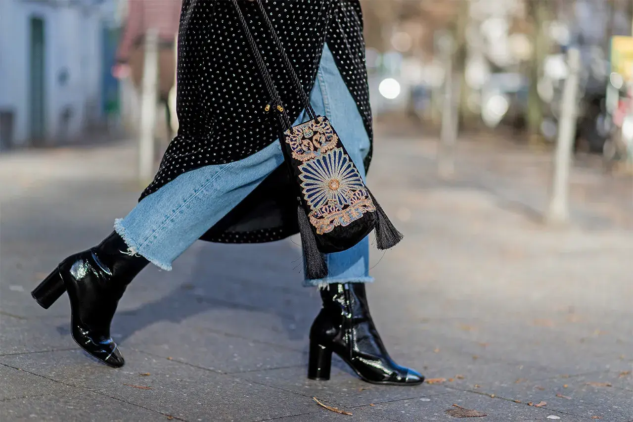 Estilo urbano: cómo combinar botines negros brillantes con jeans desgastados y un bolso bordado.