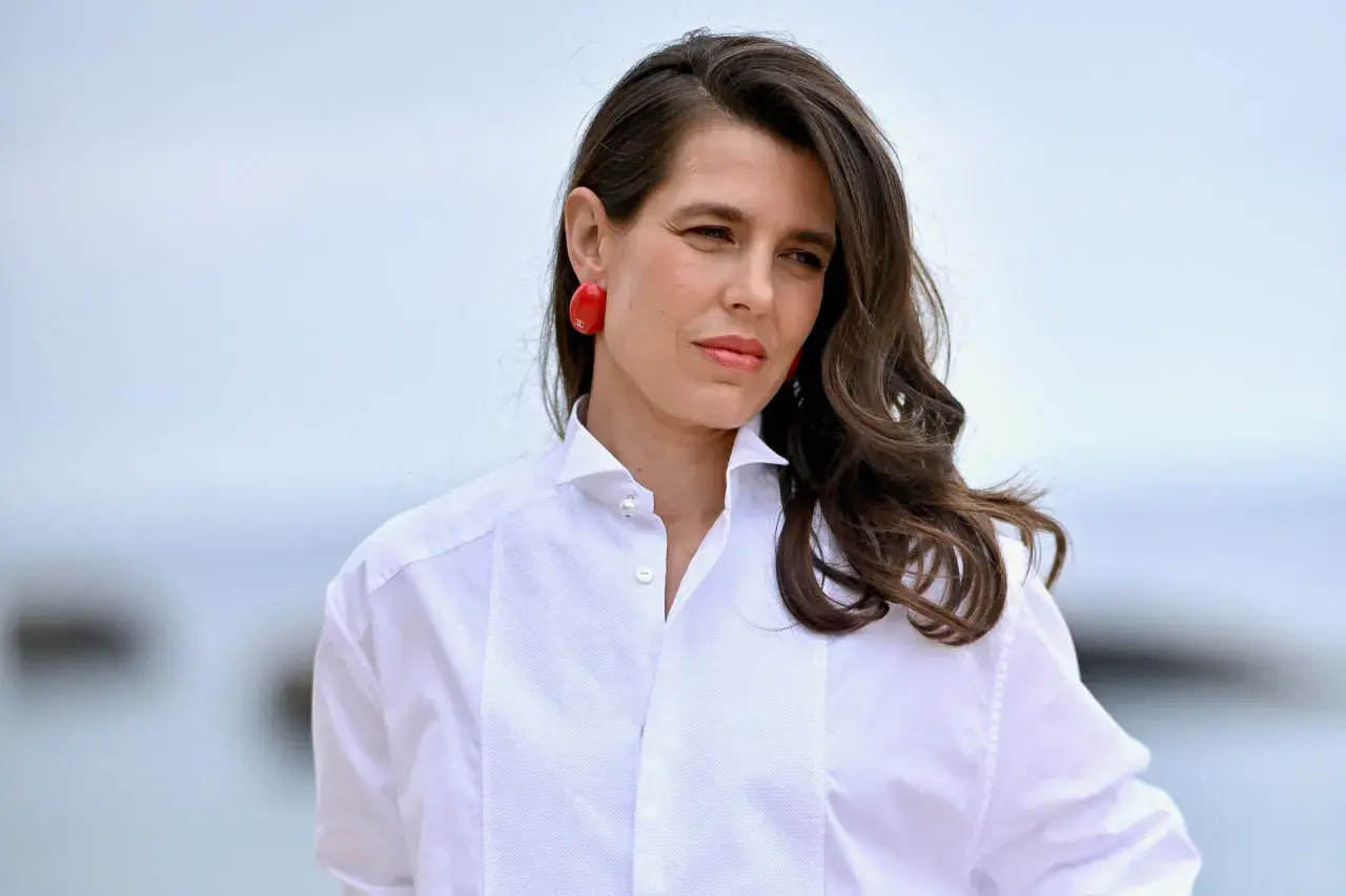 Carlota de Monaco, con pendientes rojos y camisa blanca, mira a lo lejos.