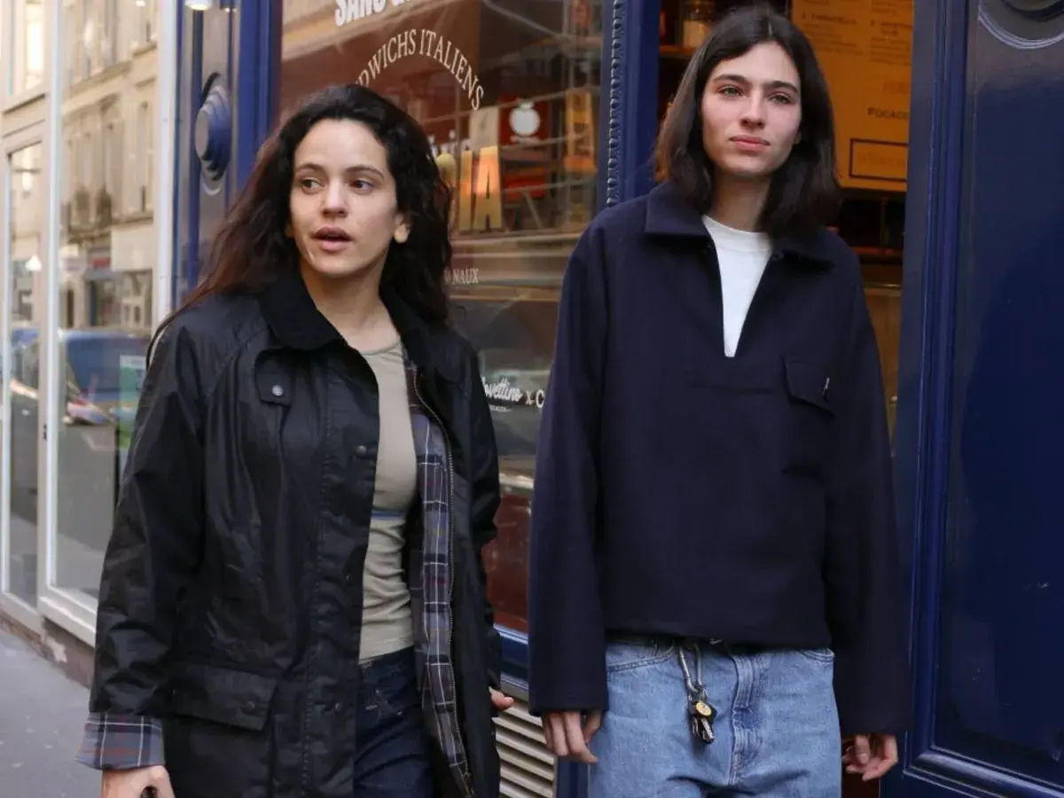 Dos jóvenes pasean por una calle, uno con chaqueta negra y el otro con jersey azul marino. Quizás buscando la loli bahía.