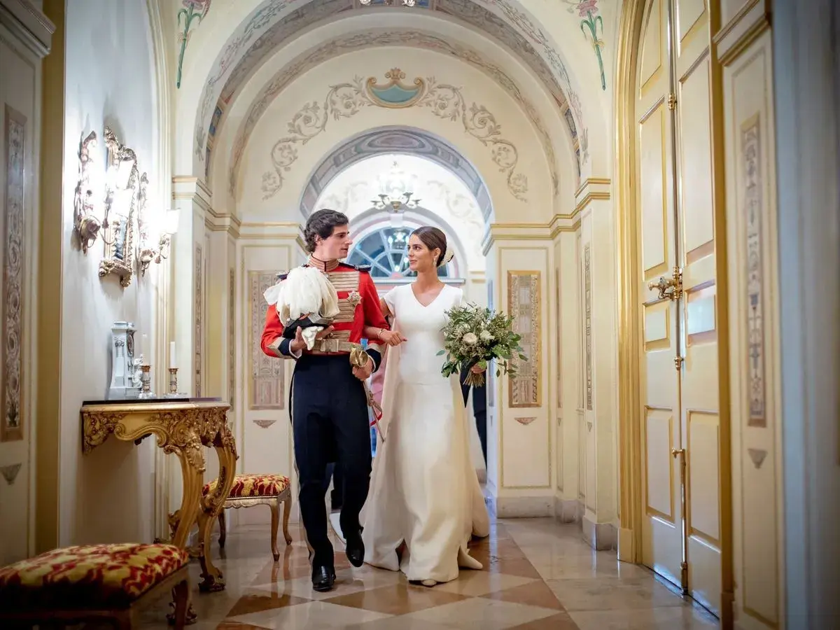 Sofía Palazuelo y su esposo, con traje de gala, caminan por un pasillo adornado, celebrando su boda.