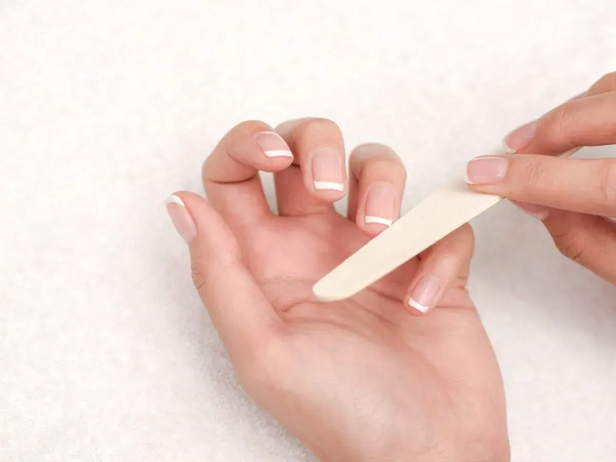 Manos limándose las uñas francesas. Una guía visual para saber como quitar uñas de gel.