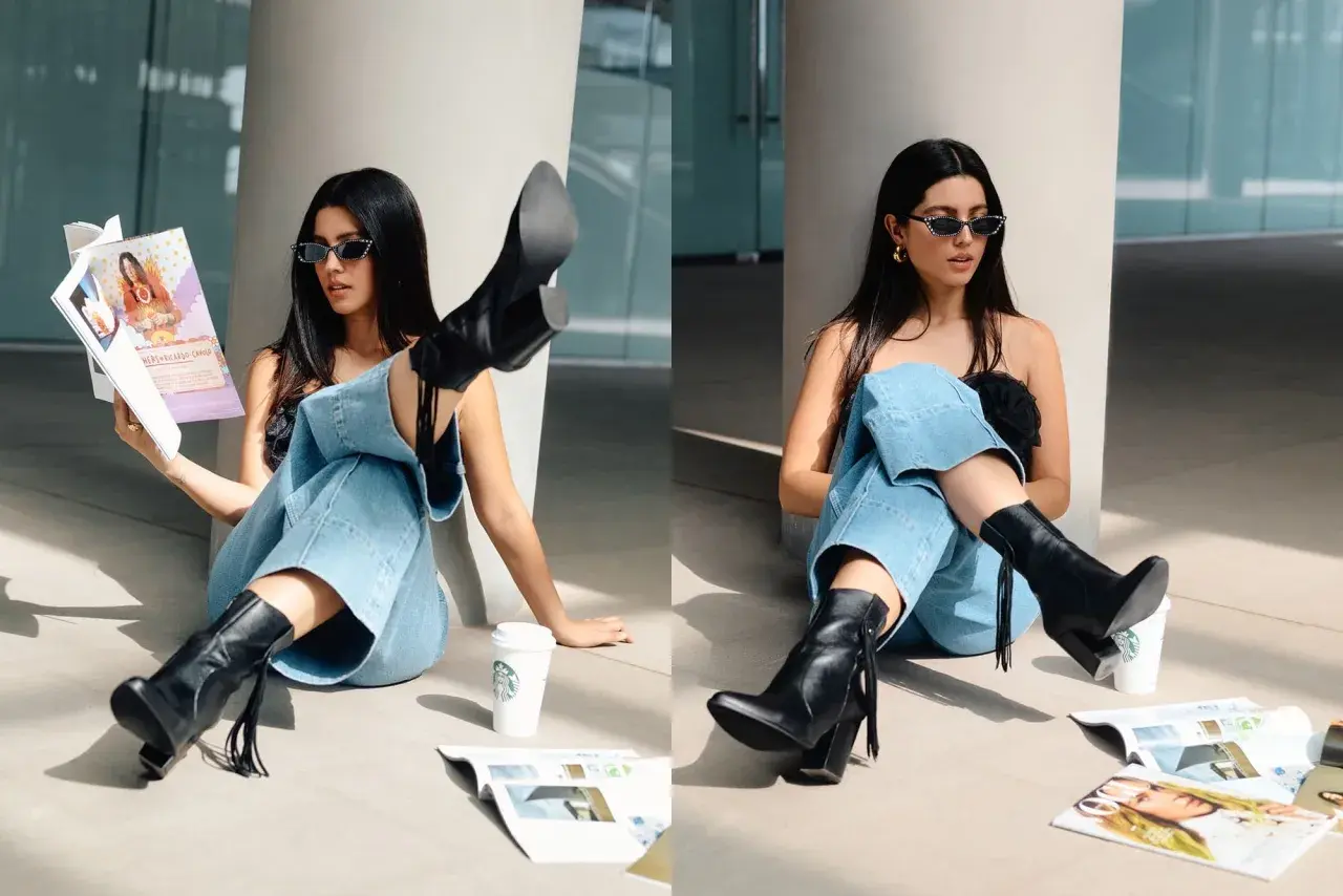 Chica con gafas de sol y jeans anchos, luciendo unas **botas en verano** mientras lee una revista junto a un café.