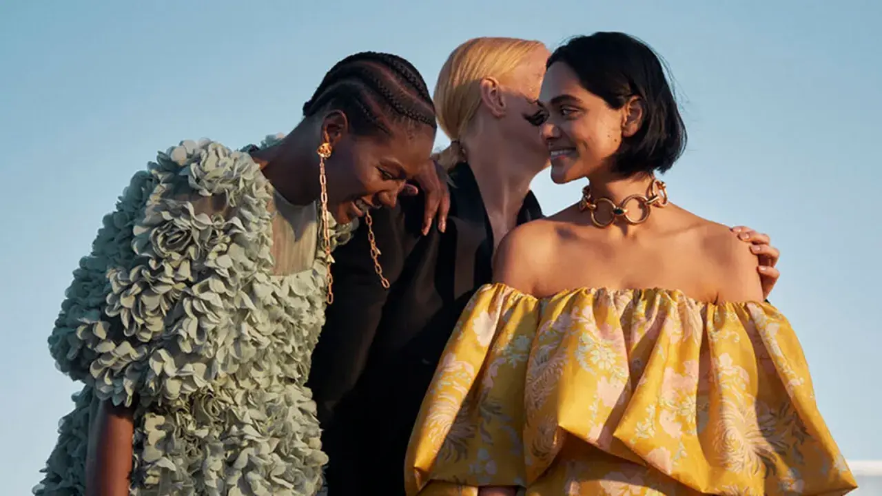 Tres mujeres ríen, una con un vestido verde con flores, otra con un collar dorado y un vestido amarillo estampado. Moda ecofriendly que es.